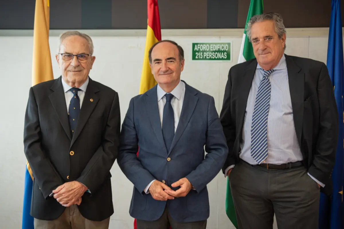 Tres hombres de traje posan juntos frente a varias banderas en un entorno formal