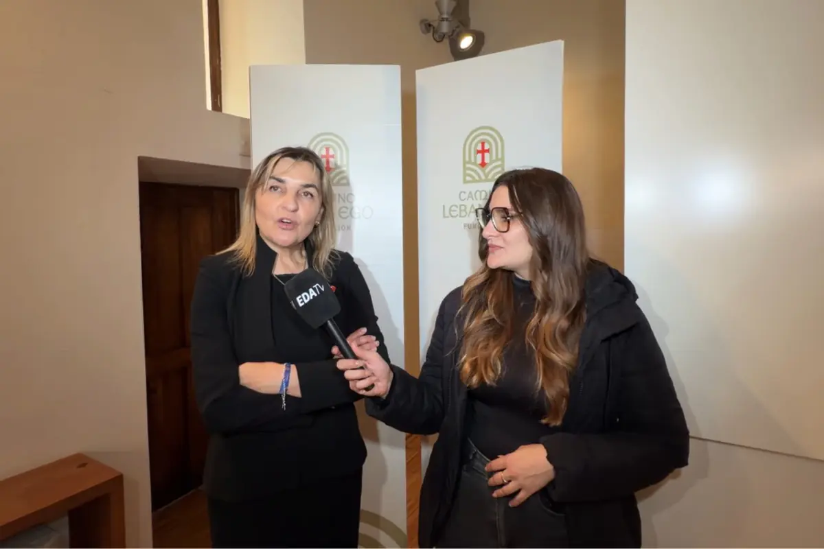 Periodista entrevistando a una mujer en un interior con paneles del Camino Lebaniego de fondo mientras sostiene un micrófono de EDATV