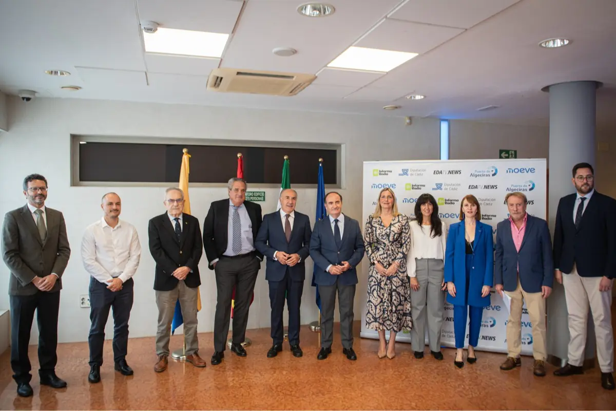 Un grupo de personas vestidas de manera formal posando para una foto en un evento institucional con banderas y un fondo con logotipos de diferentes organizaciones.