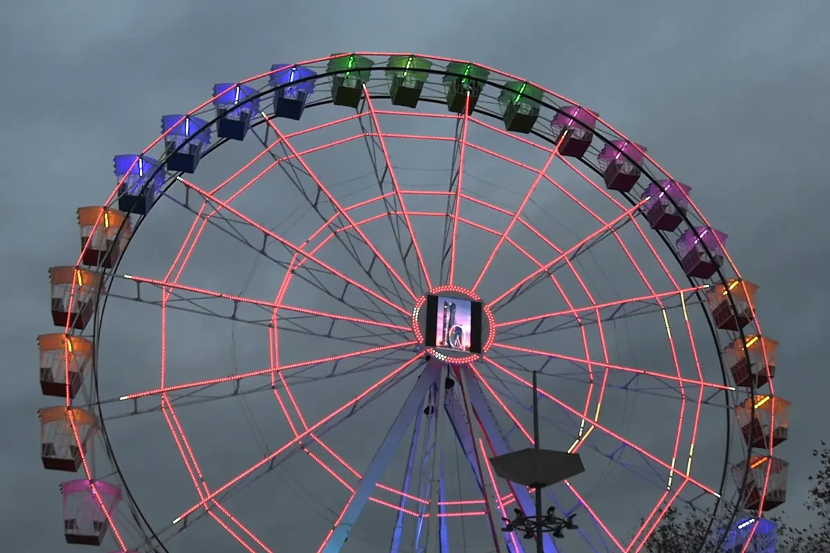 Noria gigante iluminada con luces de colores encendida al atardecer bajo un cielo nublado