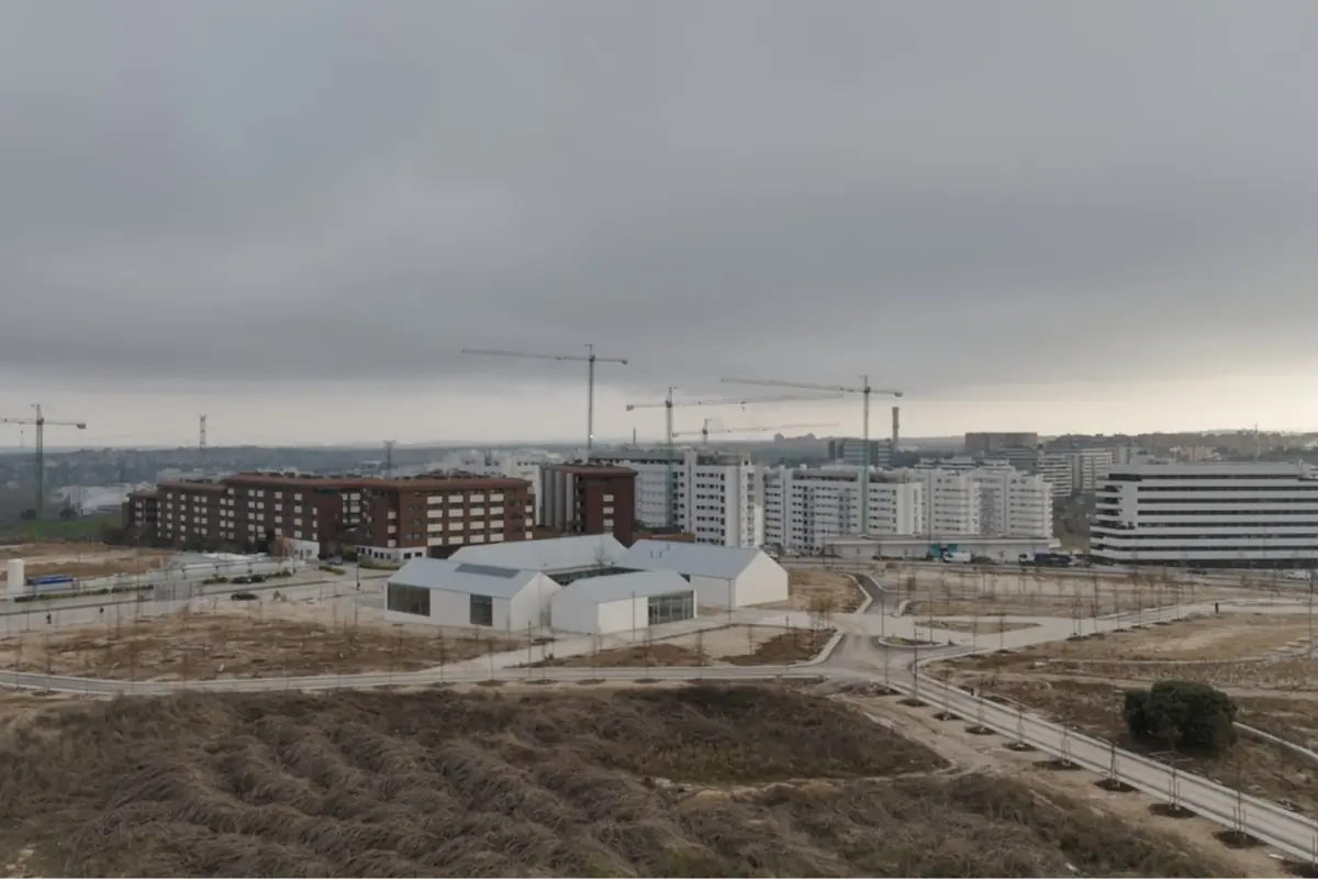 Barrio en expansión con edificios de viviendas modernos grúas de construcción y un gran edificio blanco en primer plano bajo un cielo nublado