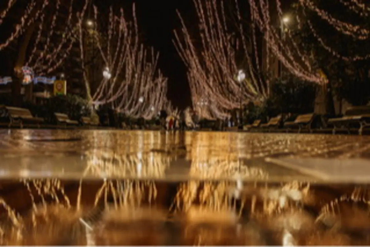 Calle nocturna con luces navideñas colgando de los árboles reflejadas en el suelo mojado