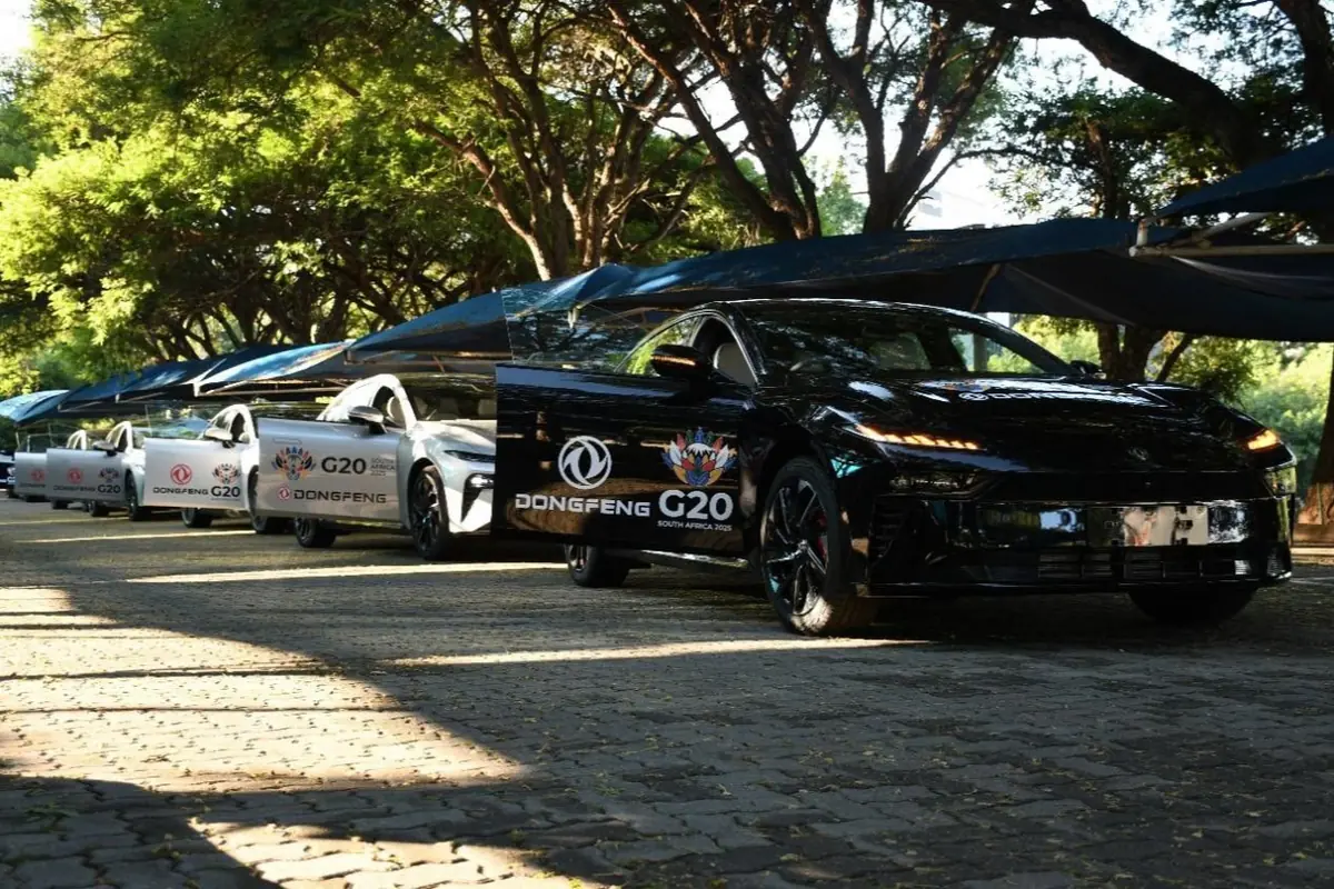 Varios autos eléctricos Dongfeng alineados bajo toldos en un entorno arbolado, con logotipos de G20 y Sudáfrica 2023 en las puertas.