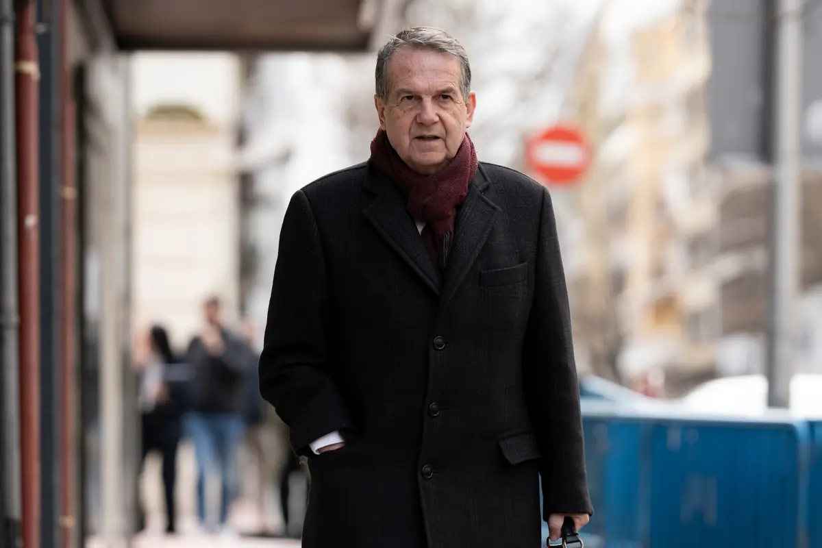 Hombre mayor con abrigo oscuro y bufanda burdeos caminando por una calle urbana en invierno