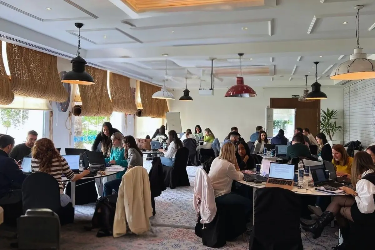 Personas trabajando en grupo en una sala iluminada con varias mesas y computadoras portátiles
