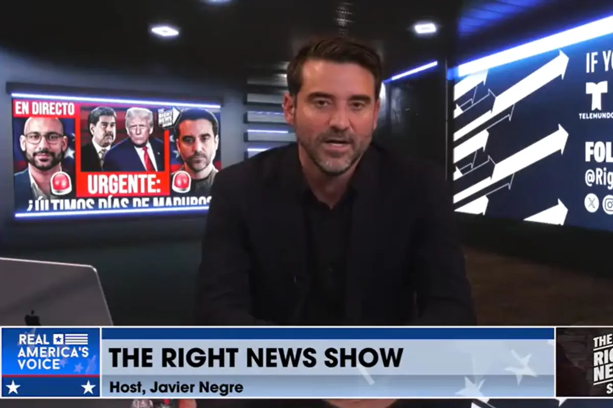 Un hombre de cabello oscuro y barba corta presenta un programa de noticias en un estudio moderno con pantallas que muestran gráficos y titulares llamativos sobre política internacional.