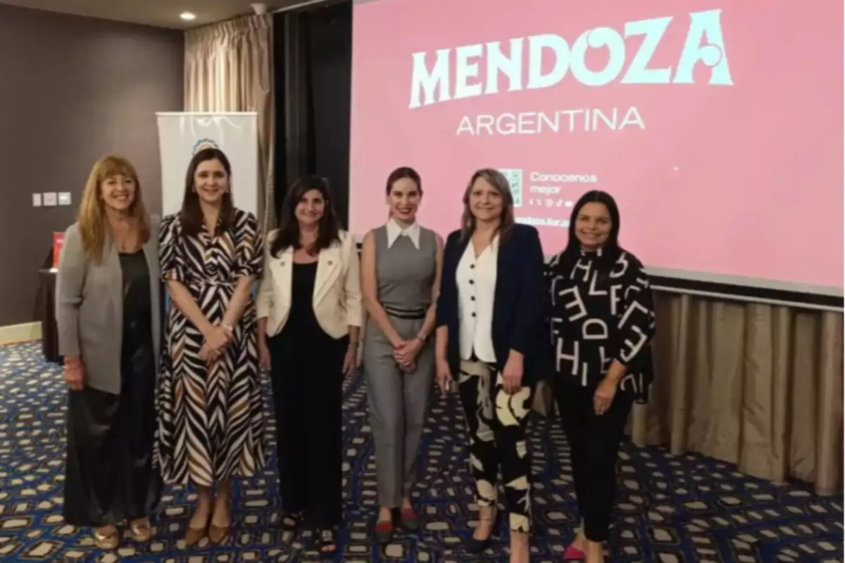 Seis mujeres posan sonrientes en un salón alfombrado con una pantalla de fondo que muestra la palabra Mendoza y Argentina