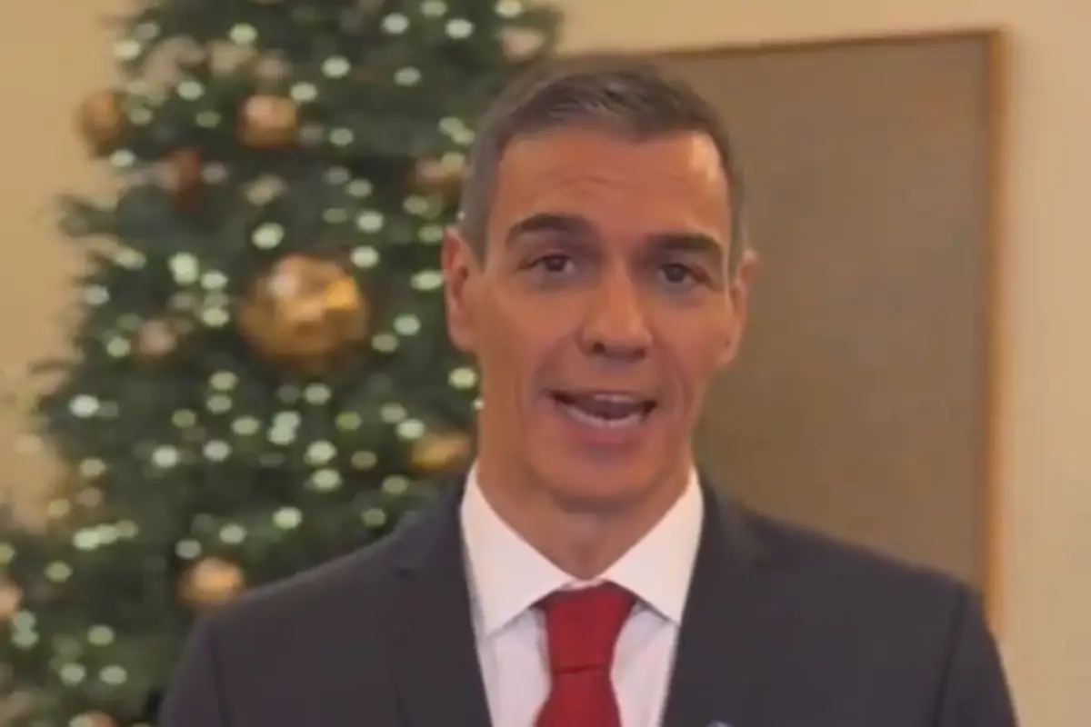 Hombre con traje oscuro y corbata roja hablando frente a un árbol de Navidad decorado con luces y bolas doradas Hombre con traje oscuro y corbata roja hablando frente a un árbol de Navidad decorado con luces y bolas doradas