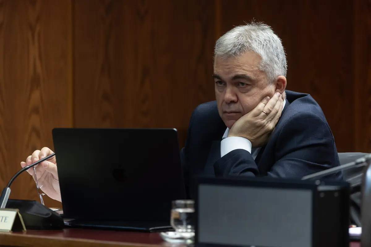 Hombre de mediana edad con traje oscuro sentado en una sala de reuniones apoyando la cara en la mano mientras mira pensativo la pantalla de un portátil negro
