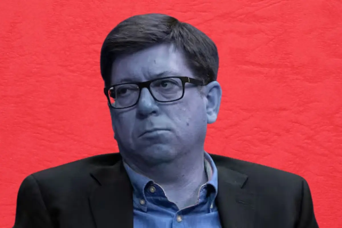 Hombre con gafas y rostro azul vistiendo saco oscuro y camisa azul sobre fondo rojo