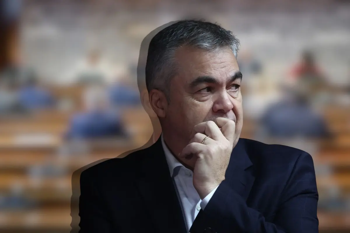 Hombre de mediana edad con traje oscuro pensativo llevándose la mano a la boca frente a un fondo de personas desenfocadas