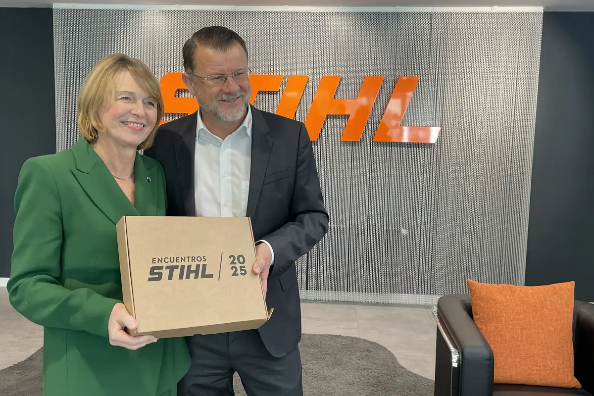 Dos personas sonríen mientras sostienen una caja de cartón con el texto Encuentros STIHL 2025 frente a un fondo con el logo de STIHL en letras naranjas