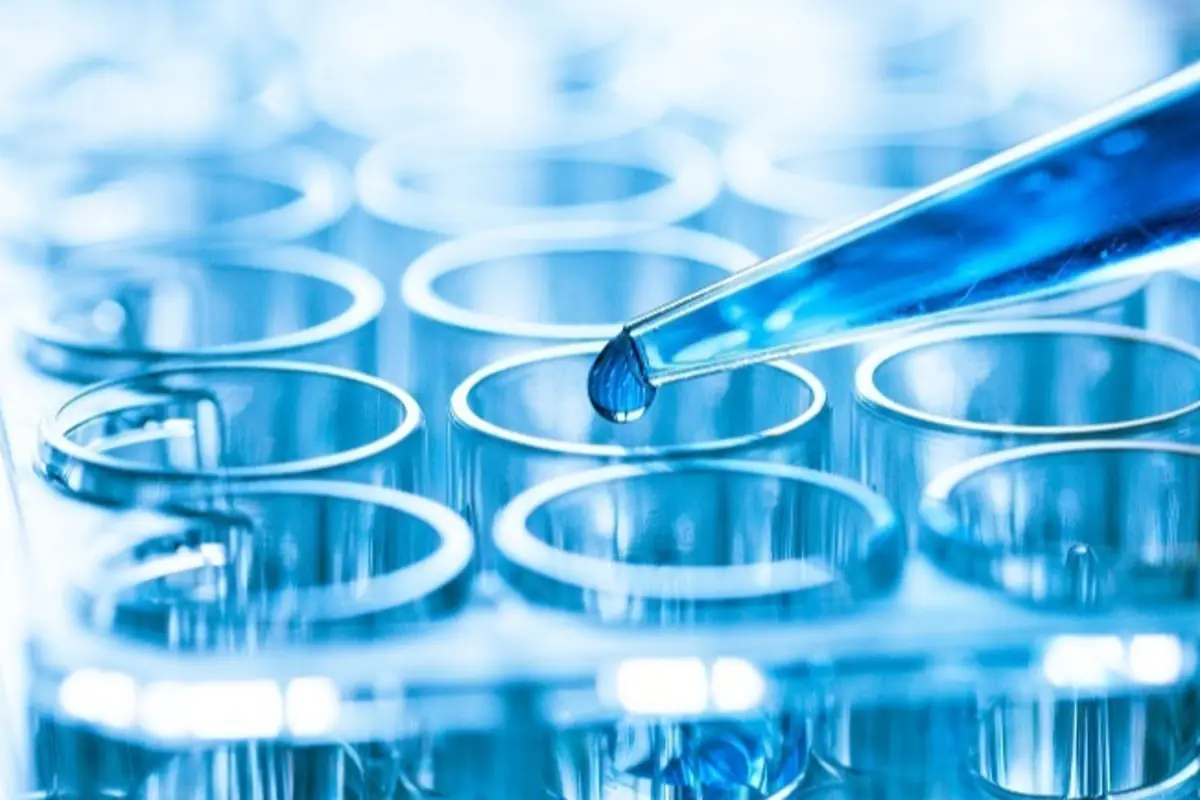 Pipeta depositando una gota de líquido azul en una bandeja de tubos de ensayo en un laboratorio científico