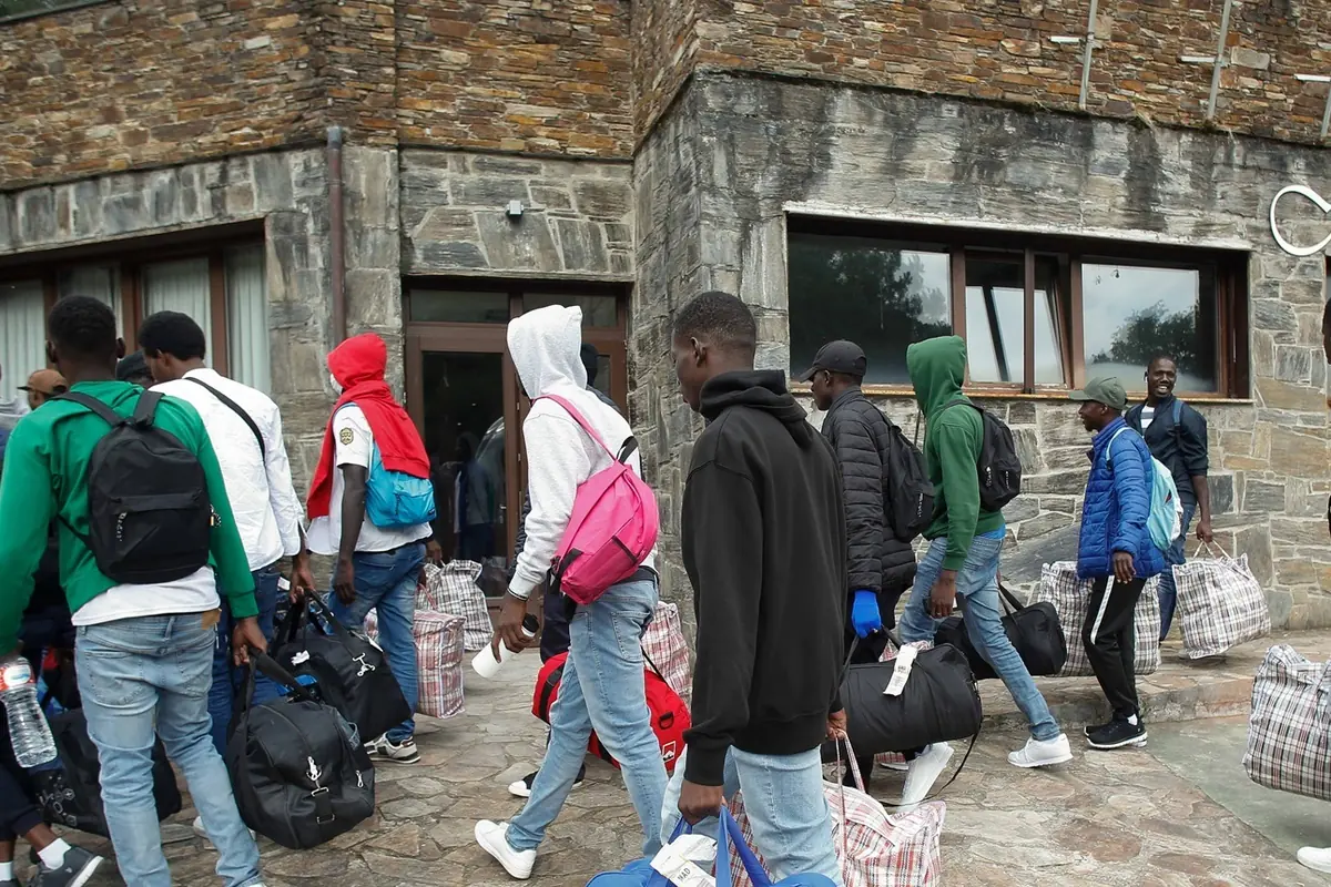 Grupo de personas jóvenes con mochilas y bolsas grandes entrando en un edificio de piedra