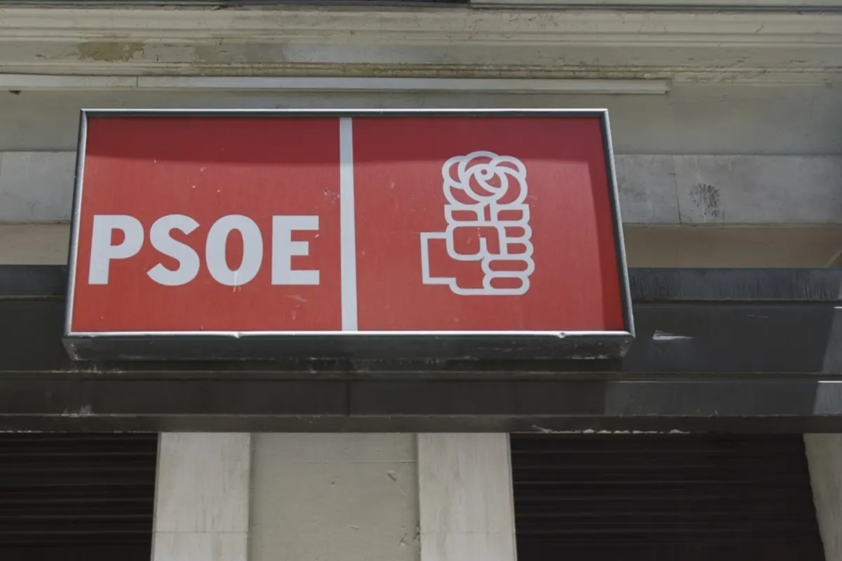 Cartel rojo con las siglas PSOE y el logotipo de un puño sosteniendo una rosa en la fachada de un edificio