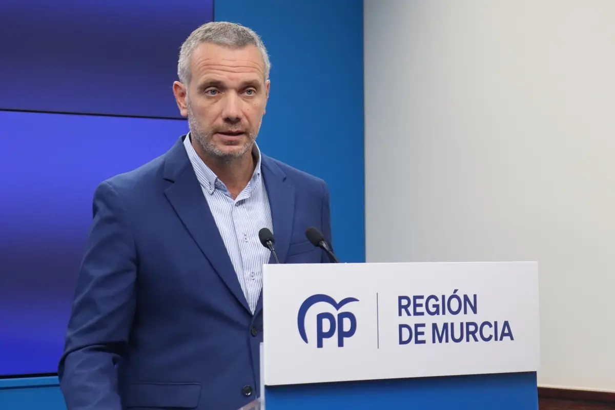 Hombre con barba y cabello corto canoso usando un traje azul habla en una conferencia de prensa frente a un atril con el logo del PP y el texto Región de Murcia Hombre con barba y cabello corto canoso usando un traje azul habla en una conferencia de prensa frente a un atril con el logo del PP y el texto Región de Murcia