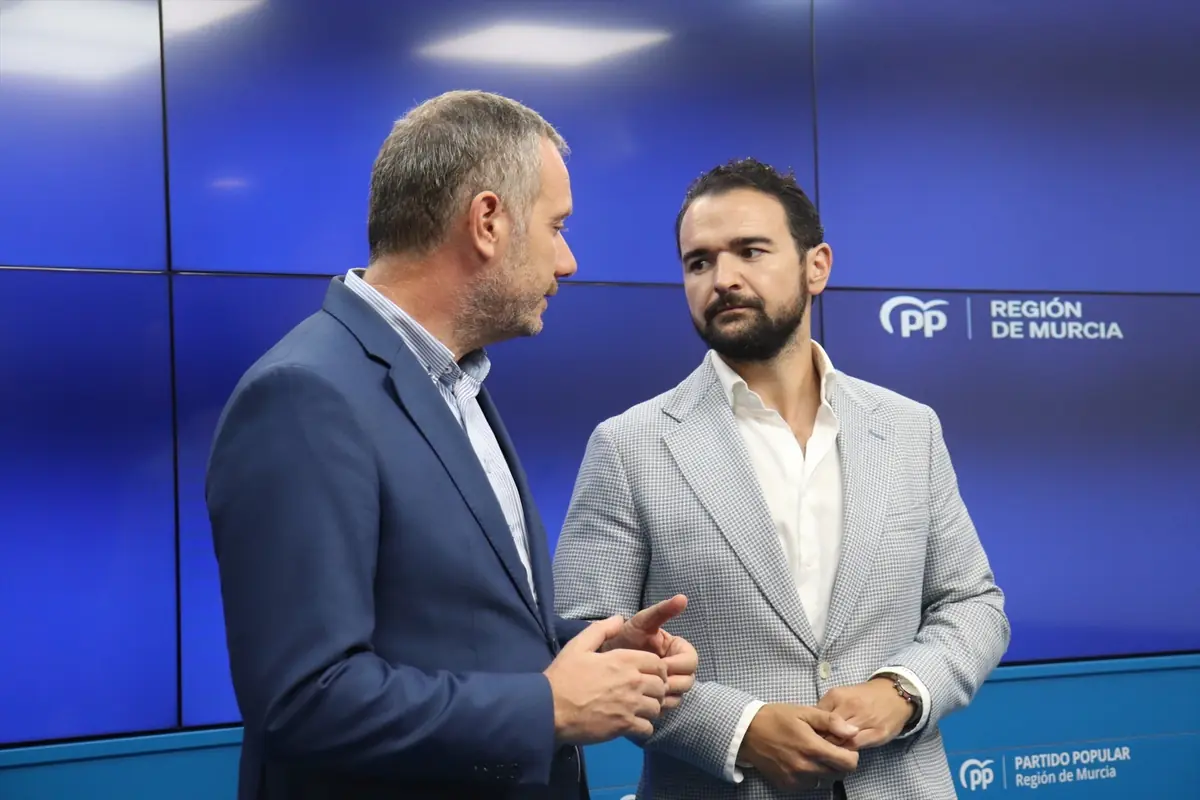 Dos hombres con traje conversan frente a un fondo azul con el logotipo del Partido Popular y la leyenda Región de Murcia. Dos hombres con traje conversan frente a un fondo azul con el logotipo del Partido Popular y la leyenda Región de Murcia.