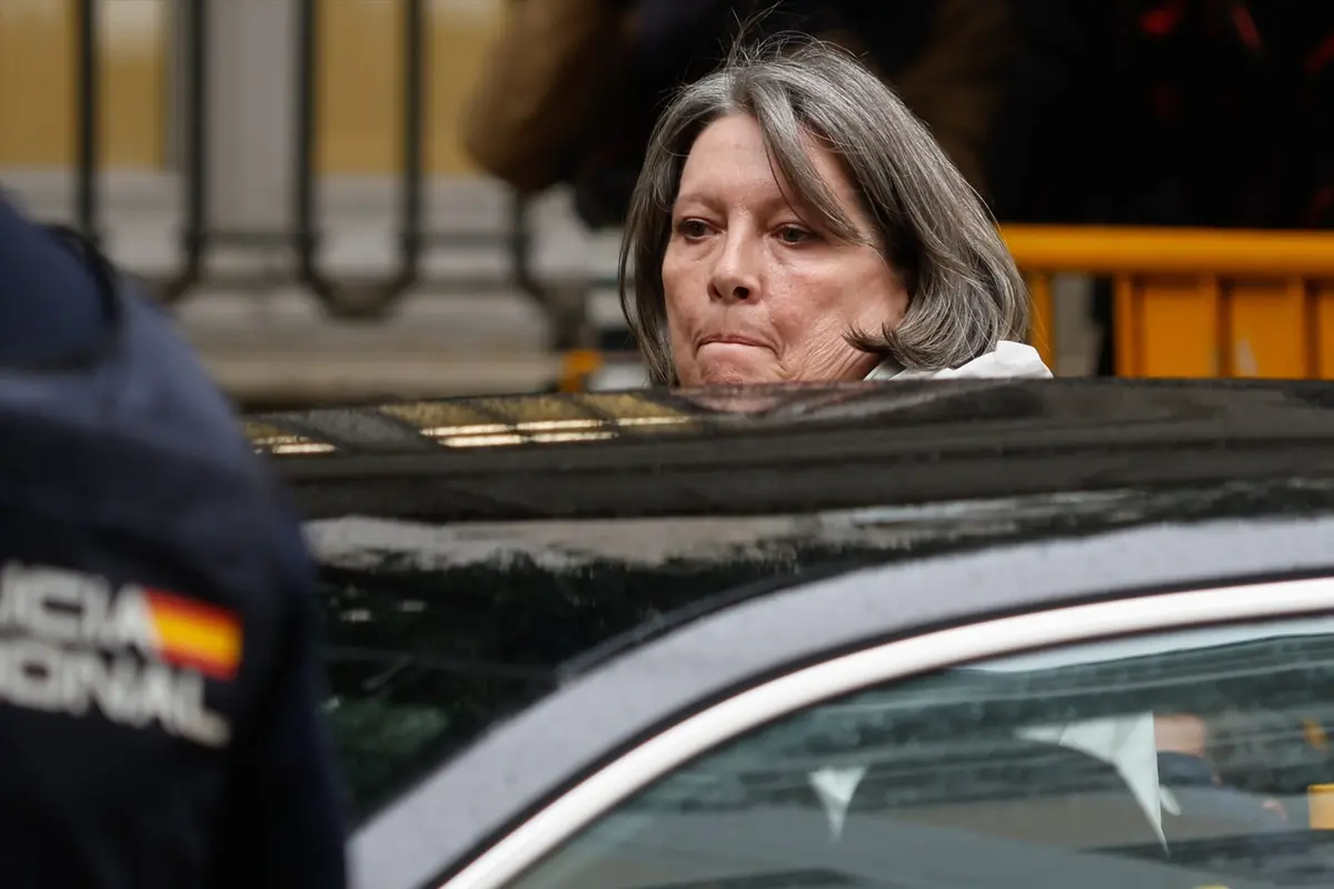 Mujer de cabello canoso subiendo a un coche escoltada por un agente de policía
