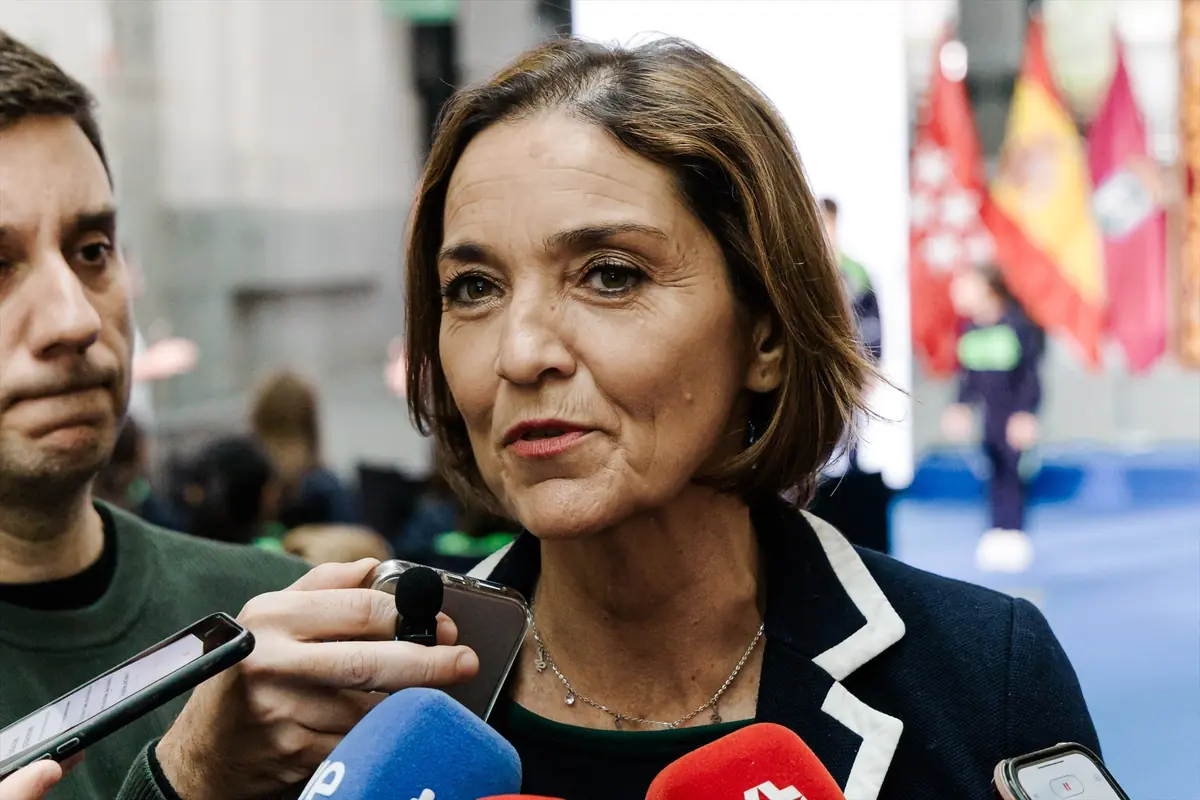 Mujer de mediana edad con micrófonos frente a ella atendiendo a la prensa en un evento con banderas de fondo Mujer de mediana edad con micrófonos frente a ella atendiendo a la prensa en un evento con banderas de fondo