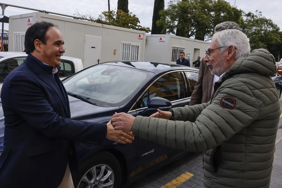 Dos hombres se saludan dándose la mano frente a un automóvil azul en un entorno urbano.