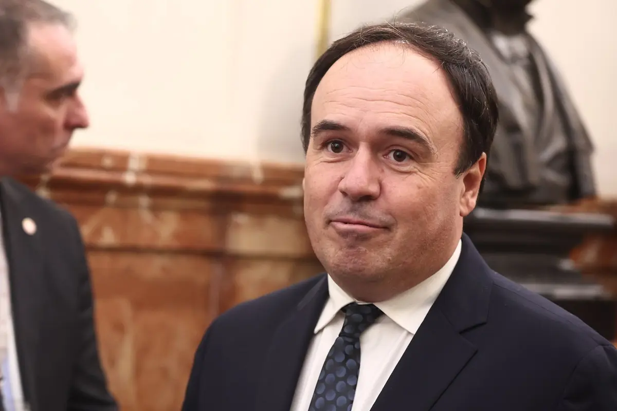 Hombre de mediana edad con traje oscuro y corbata de lunares en un entorno formal con fondo de mármol y una estatua desenfocada