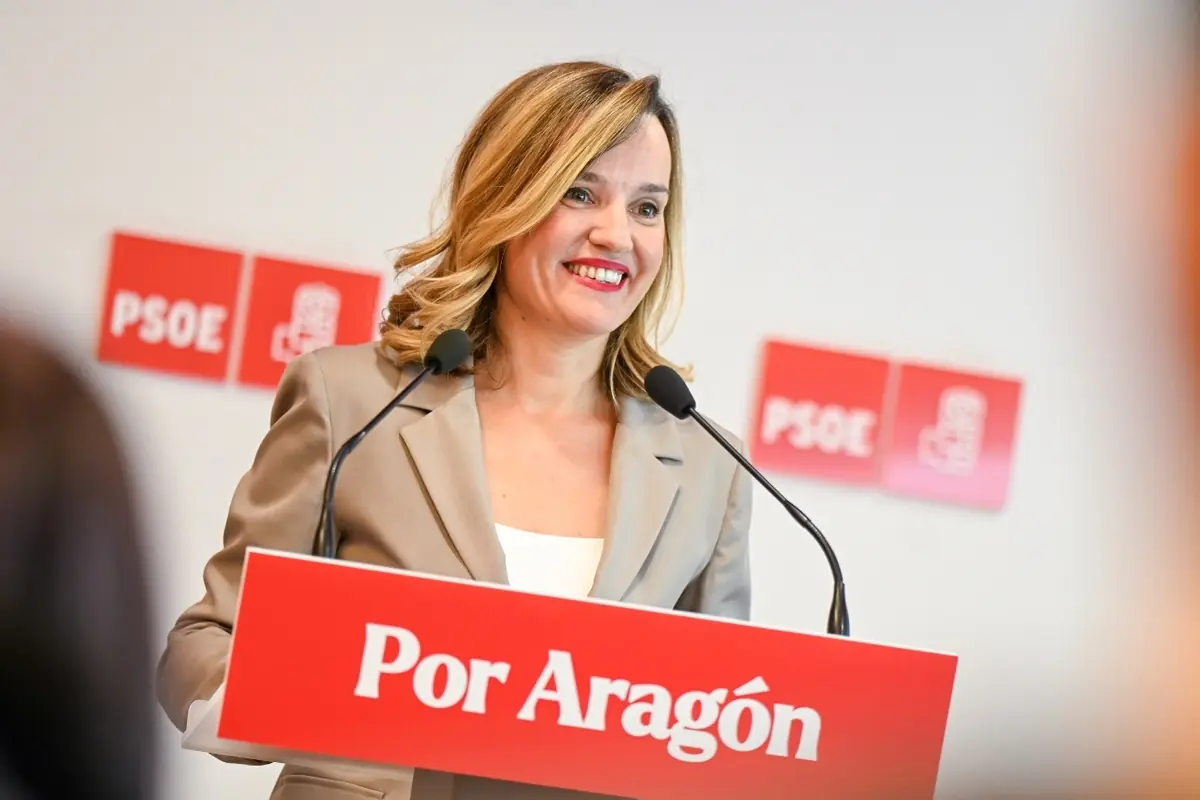 Mujer sonriente hablando en un atril con el cartel Por Aragón y logotipos de PSOE al fondo