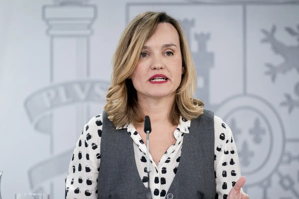 Mujer de cabello rubio y media melena hablando frente a un micrófono con fondo institucional desenfocado Mujer de cabello rubio y media melena hablando frente a un micrófono con fondo institucional desenfocado
