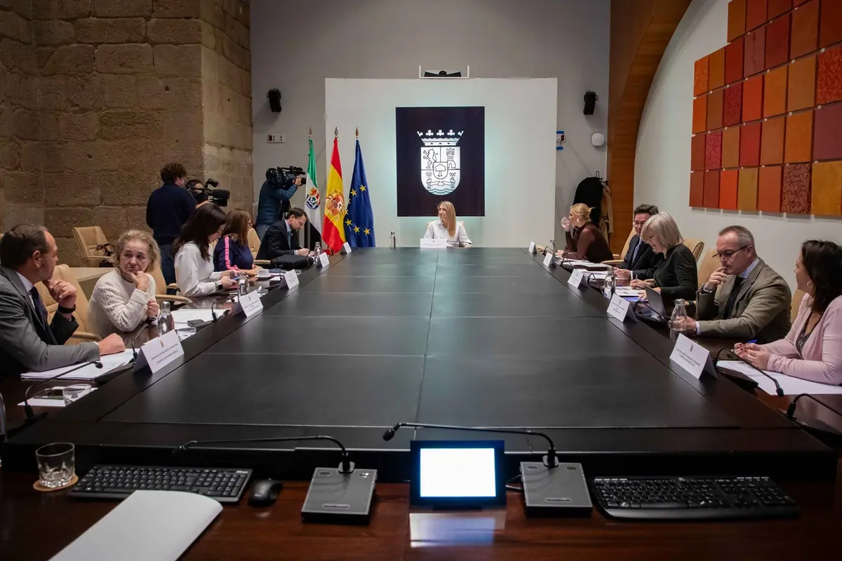 Reunión formal de varias personas sentadas alrededor de una gran mesa de conferencias en una sala con banderas oficiales y un escudo en la pared