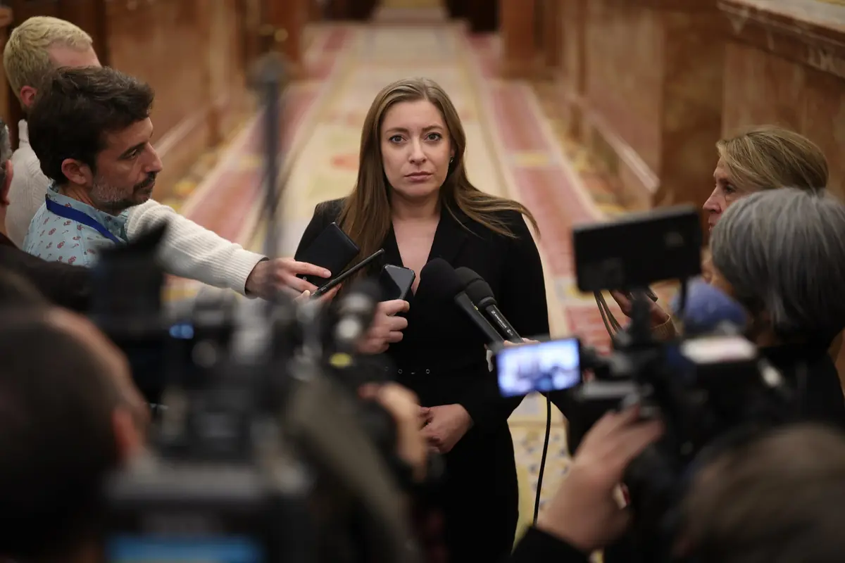 Mujer joven con gesto serio responde a periodistas y cámaras en un pasillo oficial rodeada de micrófonos y grabadoras Mujer joven con gesto serio responde a periodistas y cámaras en un pasillo oficial rodeada de micrófonos y grabadoras