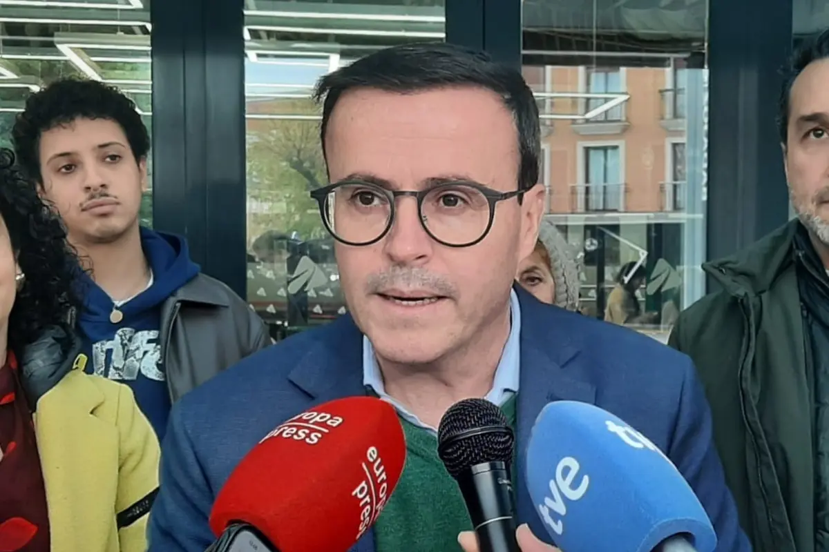 Hombre con gafas y bigote hablando ante varios micrófonos de prensa rodeado de personas en la calle