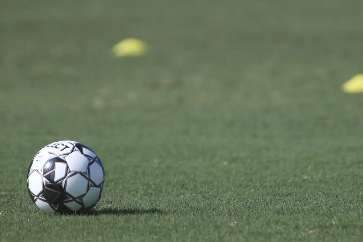 Balón de fútbol sobre césped verde con conos amarillos desenfocados al fondo