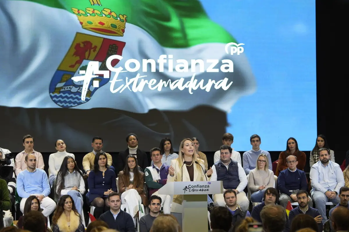 Acto político del Partido Popular en Extremadura con una oradora en un atril frente a un grupo de asistentes y una gran pantalla de fondo con la bandera de Extremadura y el lema Confianza Extremadura Acto político del Partido Popular en Extremadura con una oradora en un atril frente a un grupo de asistentes y una gran pantalla de fondo con la bandera de Extremadura y el lema Confianza Extremadura
