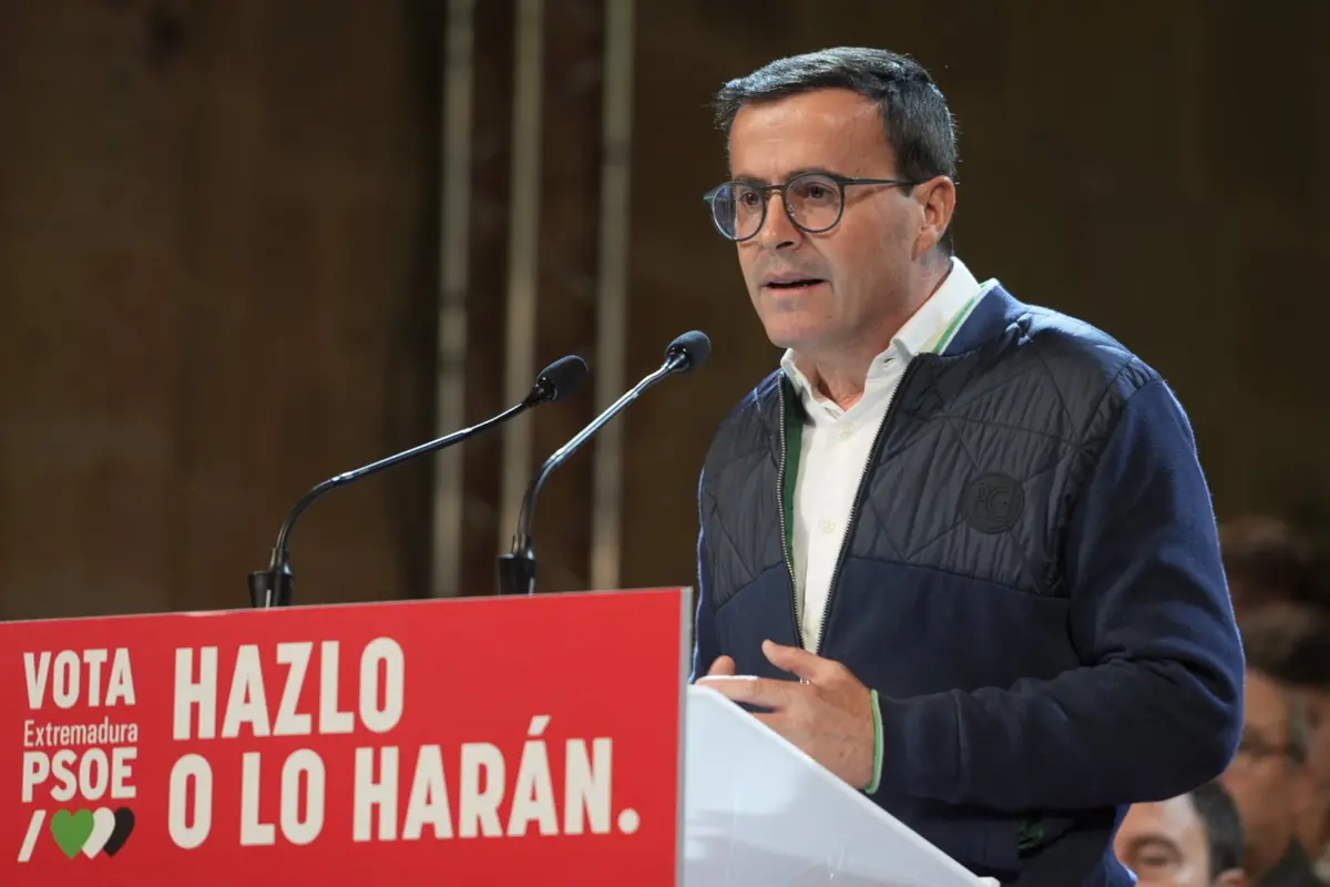 Hombre con gafas hablando en un mitin político del PSOE en Extremadura detrás de un atril rojo con el lema Hazlo o lo harán Hombre con gafas hablando en un mitin político del PSOE en Extremadura detrás de un atril rojo con el lema Hazlo o lo harán