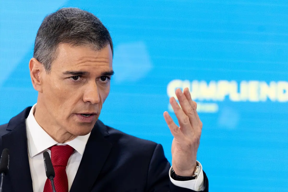 Hombre de cabello corto y canoso con traje oscuro y corbata roja hablando frente a micrófonos con fondo azul