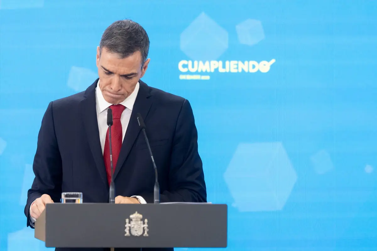 Hombre de traje oscuro y corbata roja hablando en un atril con fondo azul y la palabra cumpliendo escrita detrás