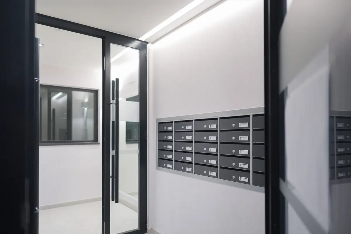 Vestíbulo moderno de edificio con puerta de vidrio y panel de buzones metálicos empotrados en la pared