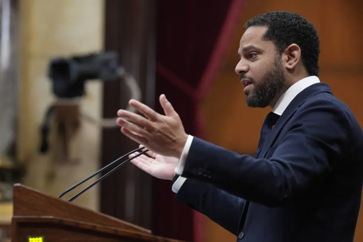 Hombre con traje oscuro hablando gesticulando con las manos desde un atril en un salón institucional