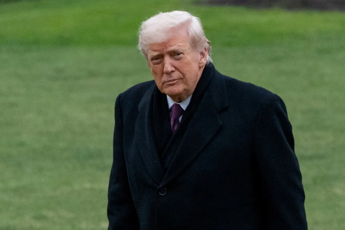 Hombre mayor de cabello claro con abrigo oscuro caminando al aire libre sobre césped verde