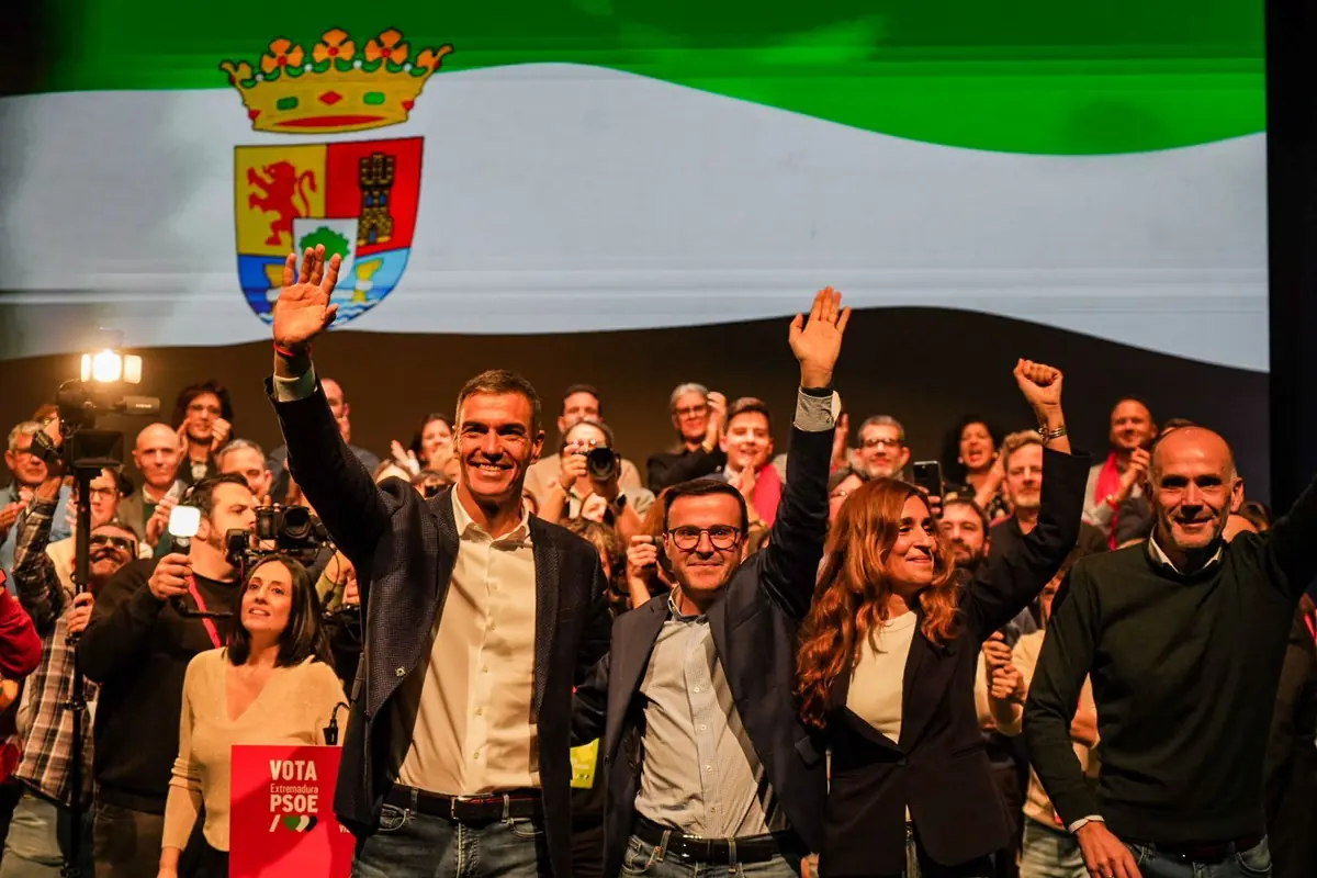 Acto de campaña del PSOE en un mitin multitudinario con dirigentes en primera fila saludando al público frente a una gran bandera de Extremadura