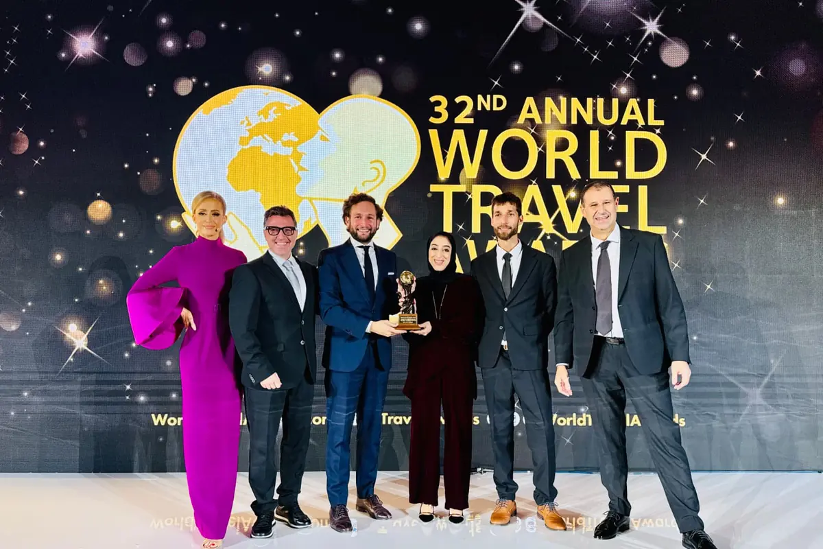 Seis personas elegantemente vestidas posan sonrientes en un escenario durante la ceremonia de los World Travel Awards, sosteniendo un trofeo frente a un fondo decorado con estrellas y el logotipo del evento.