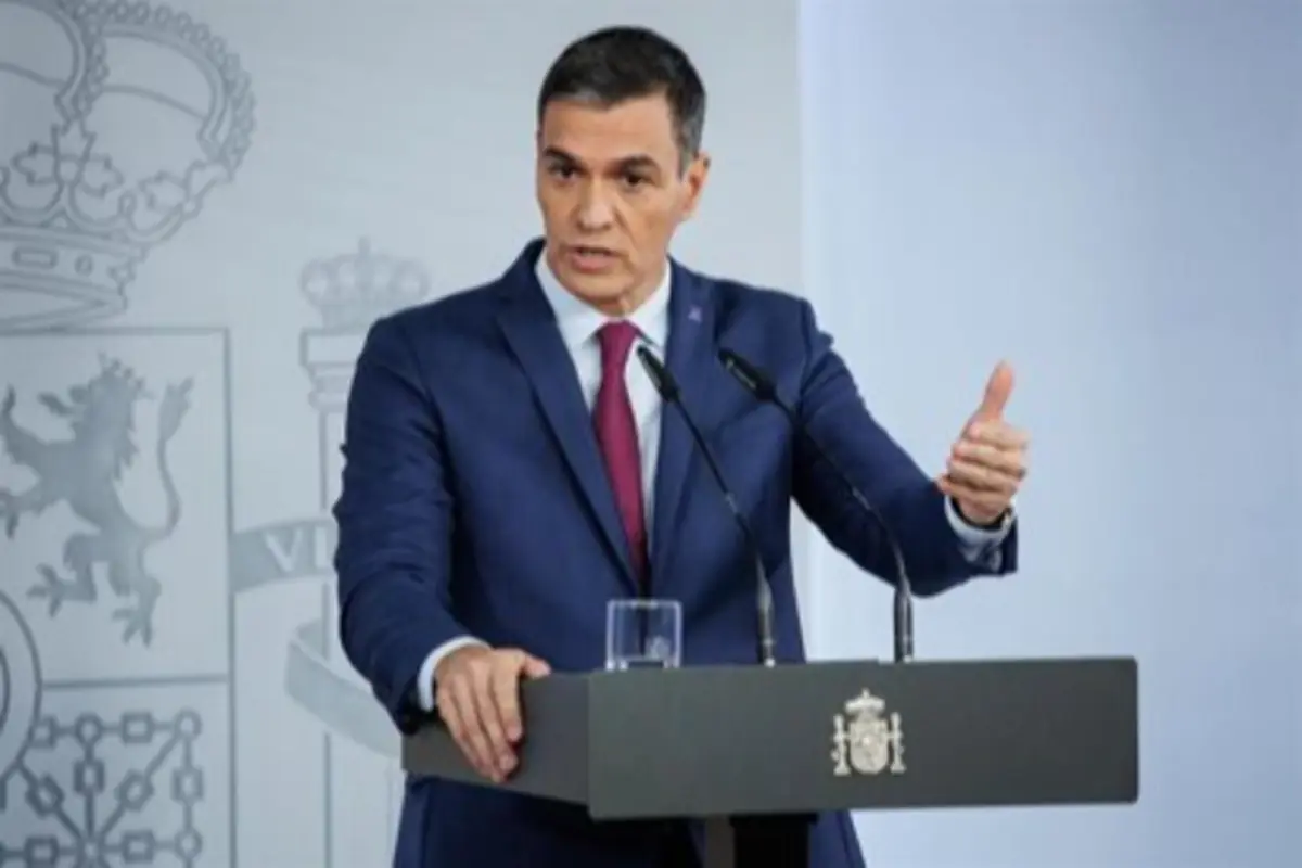 Hombre con traje azul y corbata roja hablando en una conferencia de prensa detrás de un atril con el escudo de España