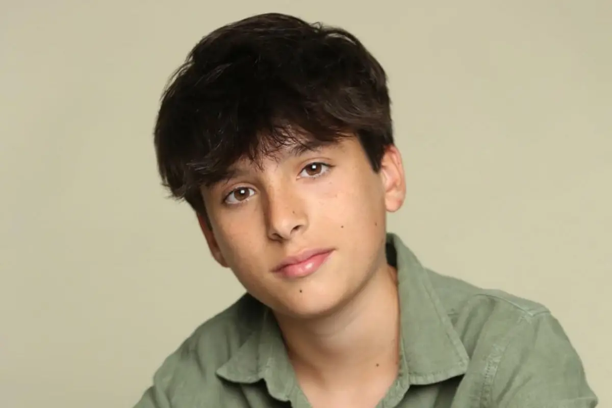 Retrato de un chico adolescente de cabello castaño oscuro y camisa verde mirando a la cámara con expresión tranquila sobre un fondo beige