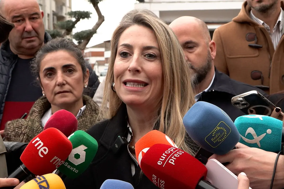 Mujer rubia hablando ante numerosos micrófonos de distintos medios de comunicación rodeada de varias personas en la calle