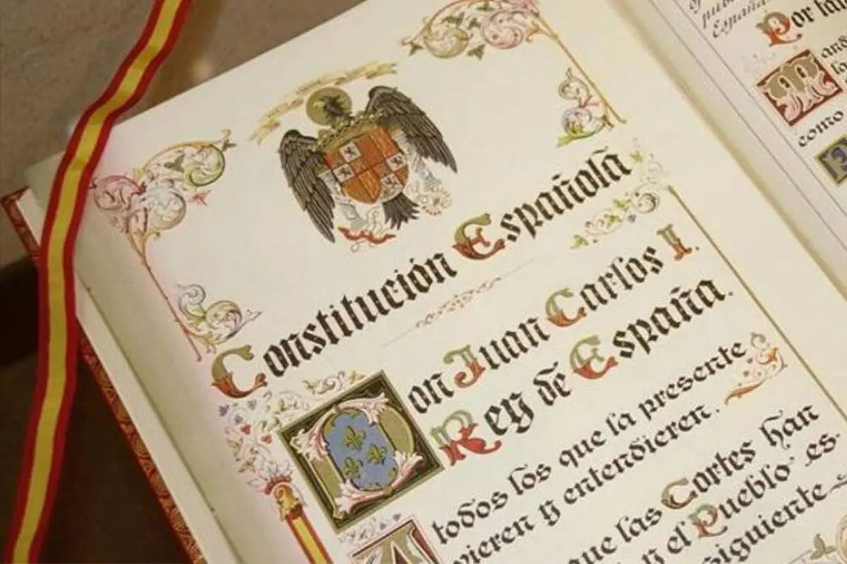 Libro antiguo de la Constitución Española con letras ornamentadas y una cinta con los colores de la bandera de España