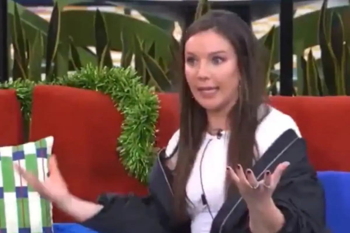 Mujer sentada en un sofá rojo gesticulando con las manos y expresión de sorpresa