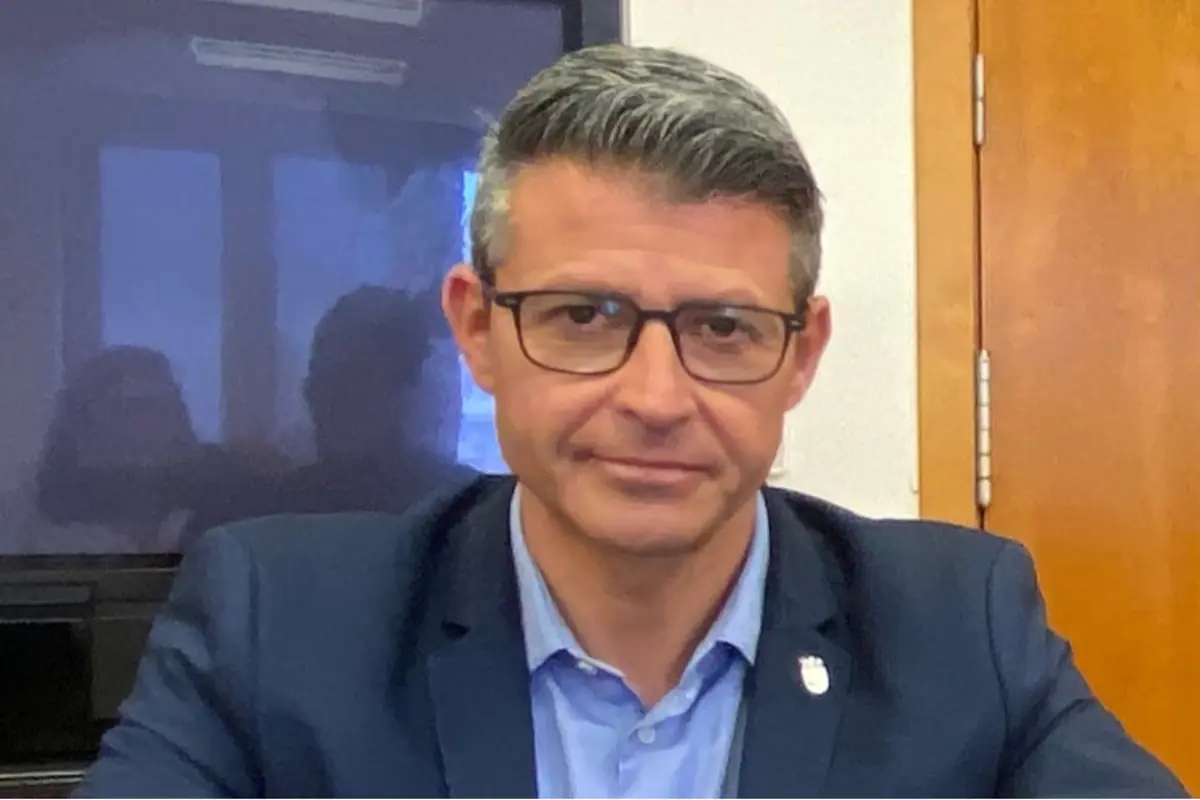 Hombre de cabello canoso y gafas con saco azul sentado frente a una puerta de madera Hombre de cabello canoso y gafas con saco azul sentado frente a una puerta de madera