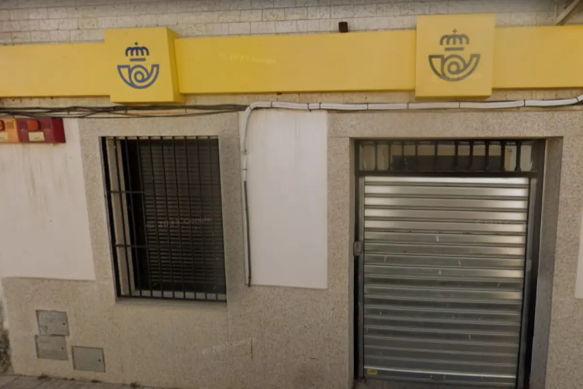 Fachada de una oficina de Correos de España con rótulo amarillo y persiana metálica cerrada