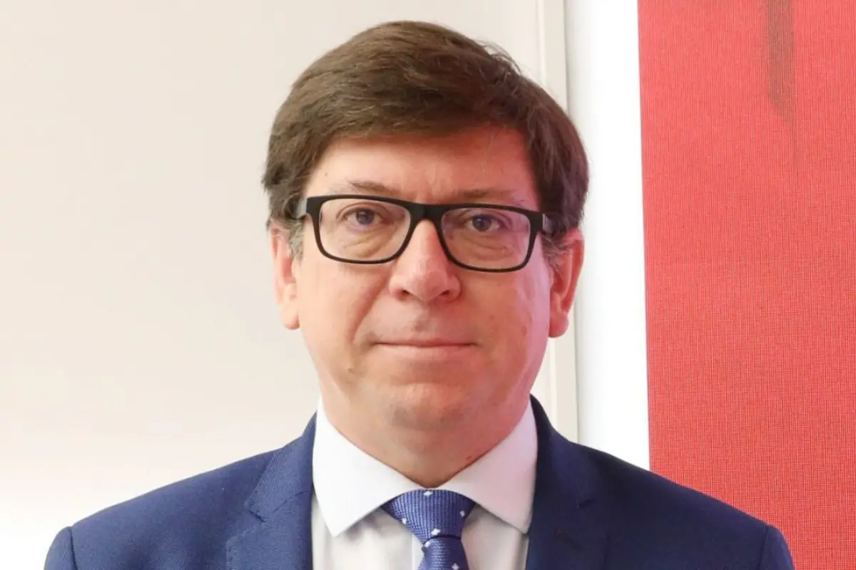 Retrato de un hombre de mediana edad con gafas y traje azul mirando a la cámara frente a un fondo blanco y rojo Retrato de un hombre de mediana edad con gafas y traje azul mirando a la cámara frente a un fondo blanco y rojo