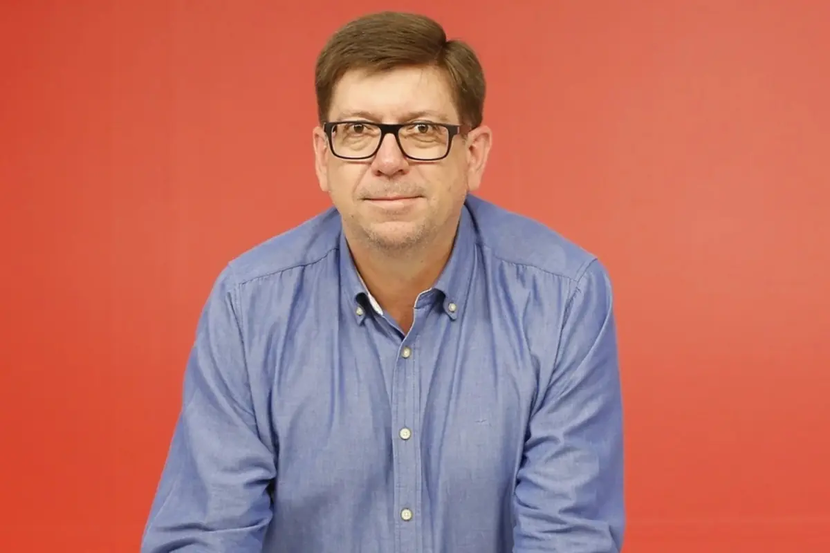 Hombre de mediana edad con gafas y camisa azul posando frente a un fondo rojo Hombre de mediana edad con gafas y camisa azul posando frente a un fondo rojo