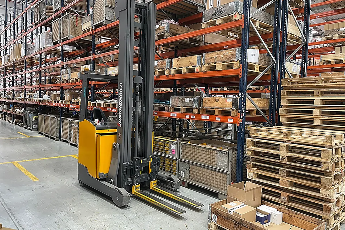 Carretilla elevadora amarilla estacionada en un almacén con estanterías altas llenas de palés y cajas